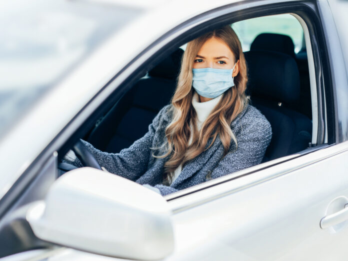 Eine junge Frau mit Schutzmaske im Auto