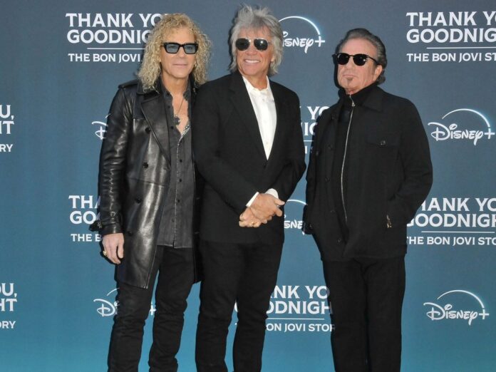 Jon Bon Jovi strahlt mit David Bryan (l.) und Tico Torres (r.) auf dem roten Teppich.